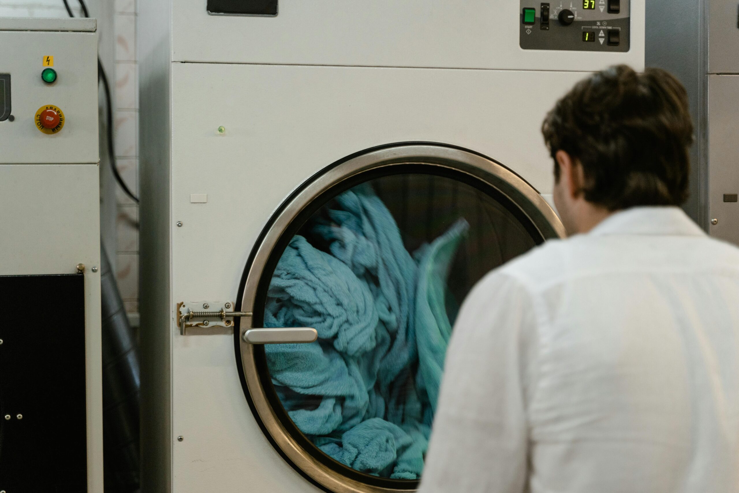 A man watches a washing machine spin in a laundromat, focusing on the process.